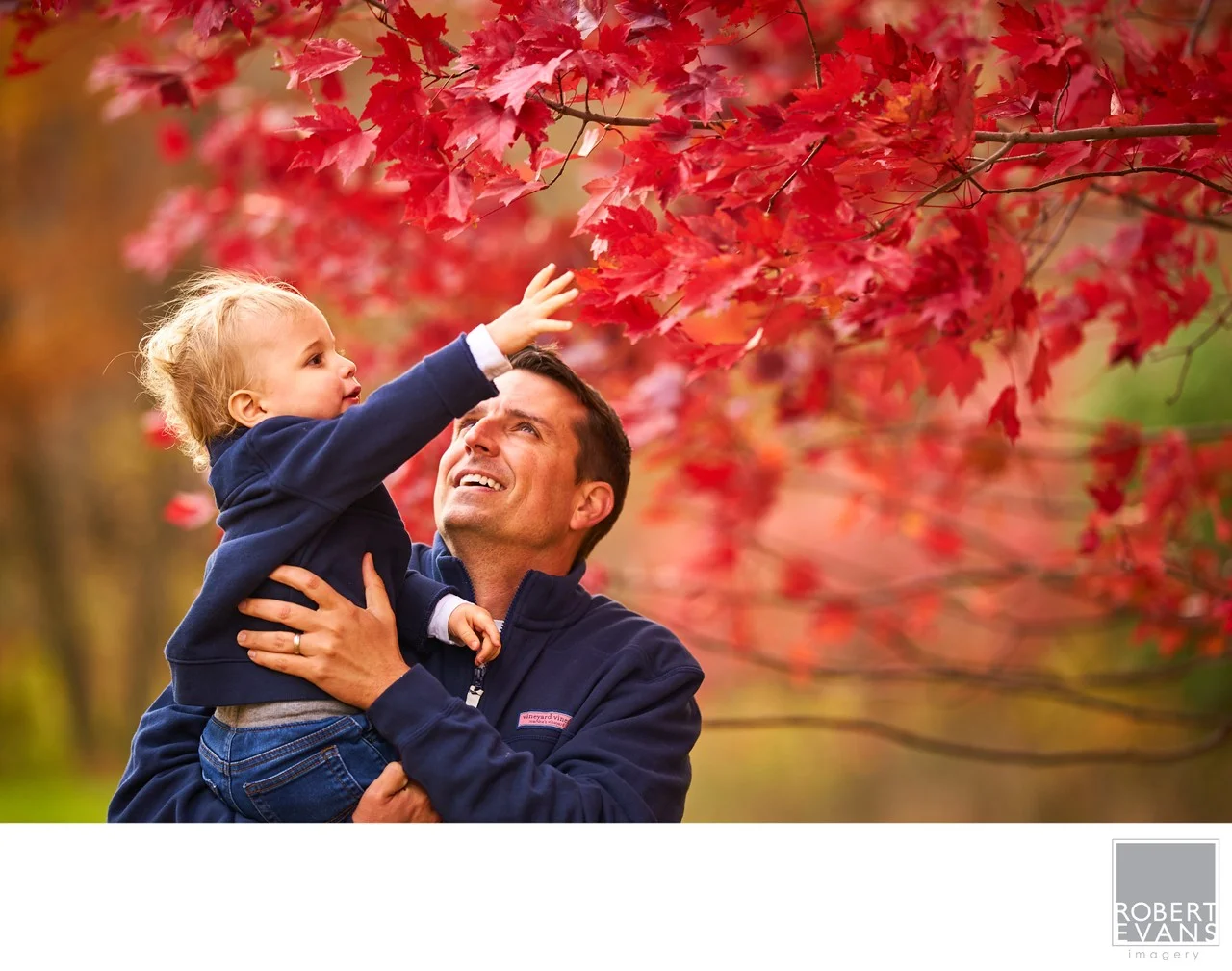 A playful father and son moment surrounded by vibrant autumn leaves, capturing the connection, laughter and personality that make family photographs meaningful.