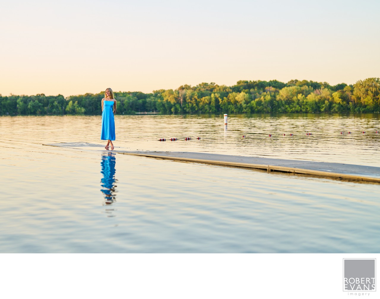 A wide lakeside portrait that uses the water, dock and evening landscape to create a sense of place while keeping the subject at the heart of the photograph.