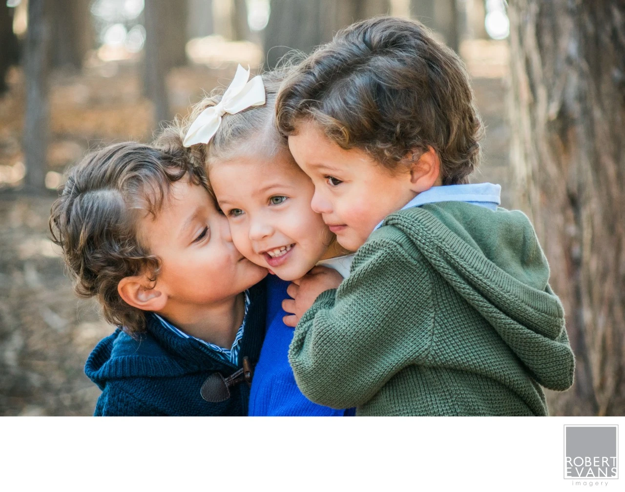 A sweet candid portrait of triplet siblings sharing a playful moment together outdoors, capturing the closeness, personality and unique bond they share.