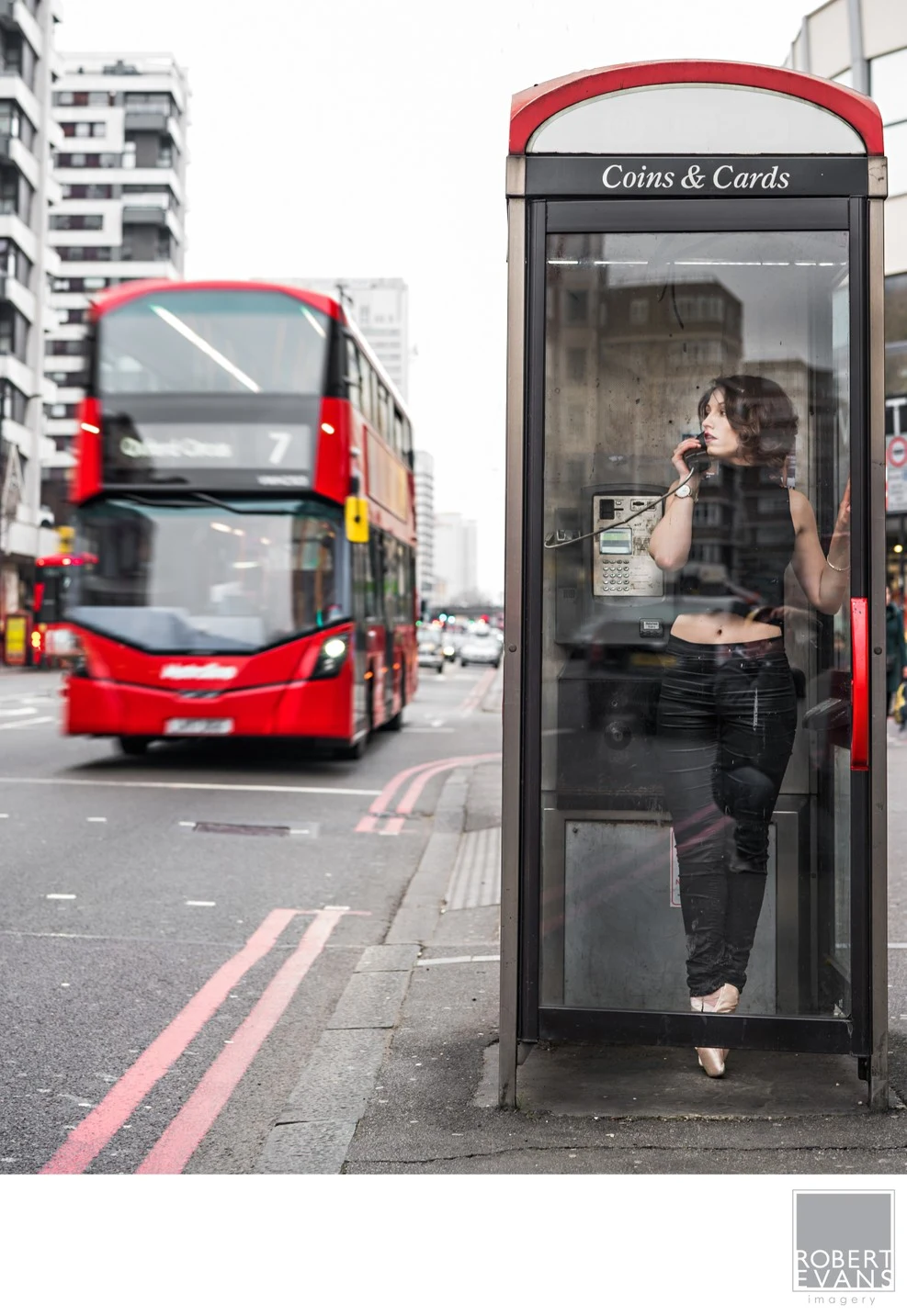 Creative environmental portrait photographed on a London street, using a classic phone booth and iconic red double-decker bus to create a distinctive urban composition.
