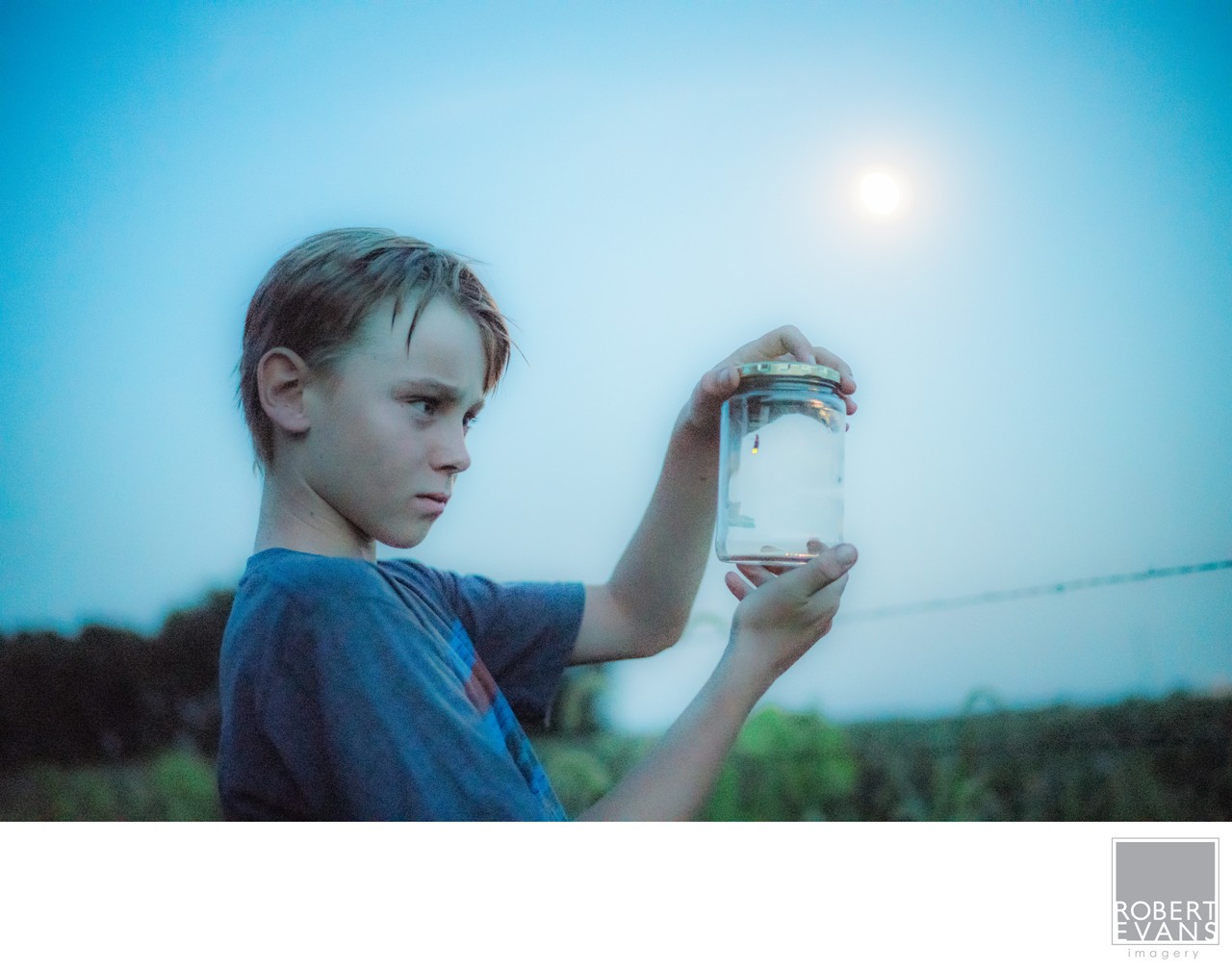 A child studies a glass jar in the blue light of evening.