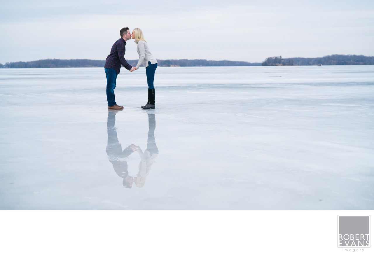 A couple kisses on a frozen lake, reflected in the ice.