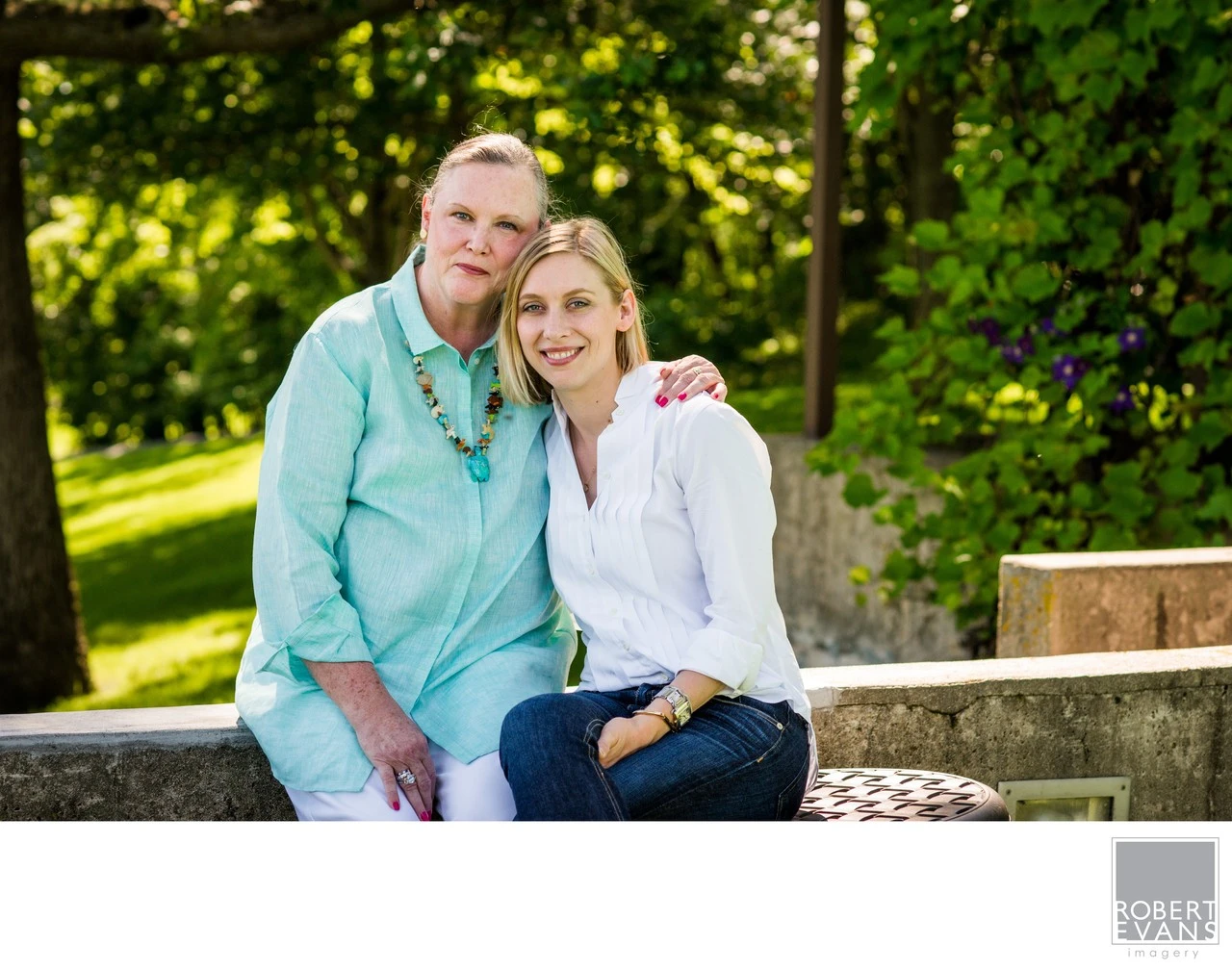 A smiling couple sits close together on a bench in a green garden.
