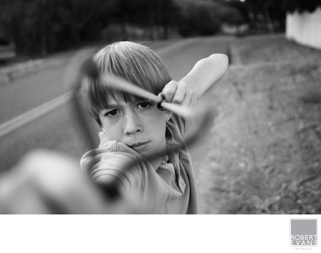 A young child concentrates while holding a toy bow outdoors in black and white.