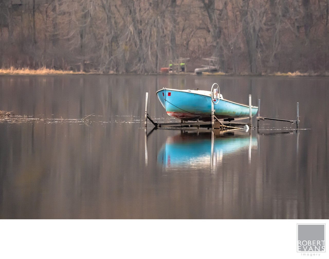 A small blue boat rests on a lift above calm water reflecting the wooded shore.