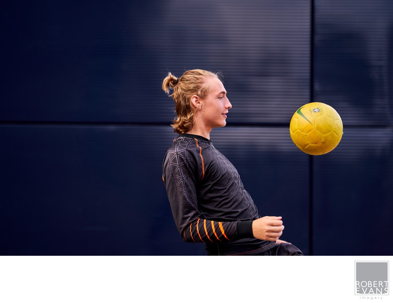 A young woman watches a yellow volleyball suspended in front of her against a dark gym wall.