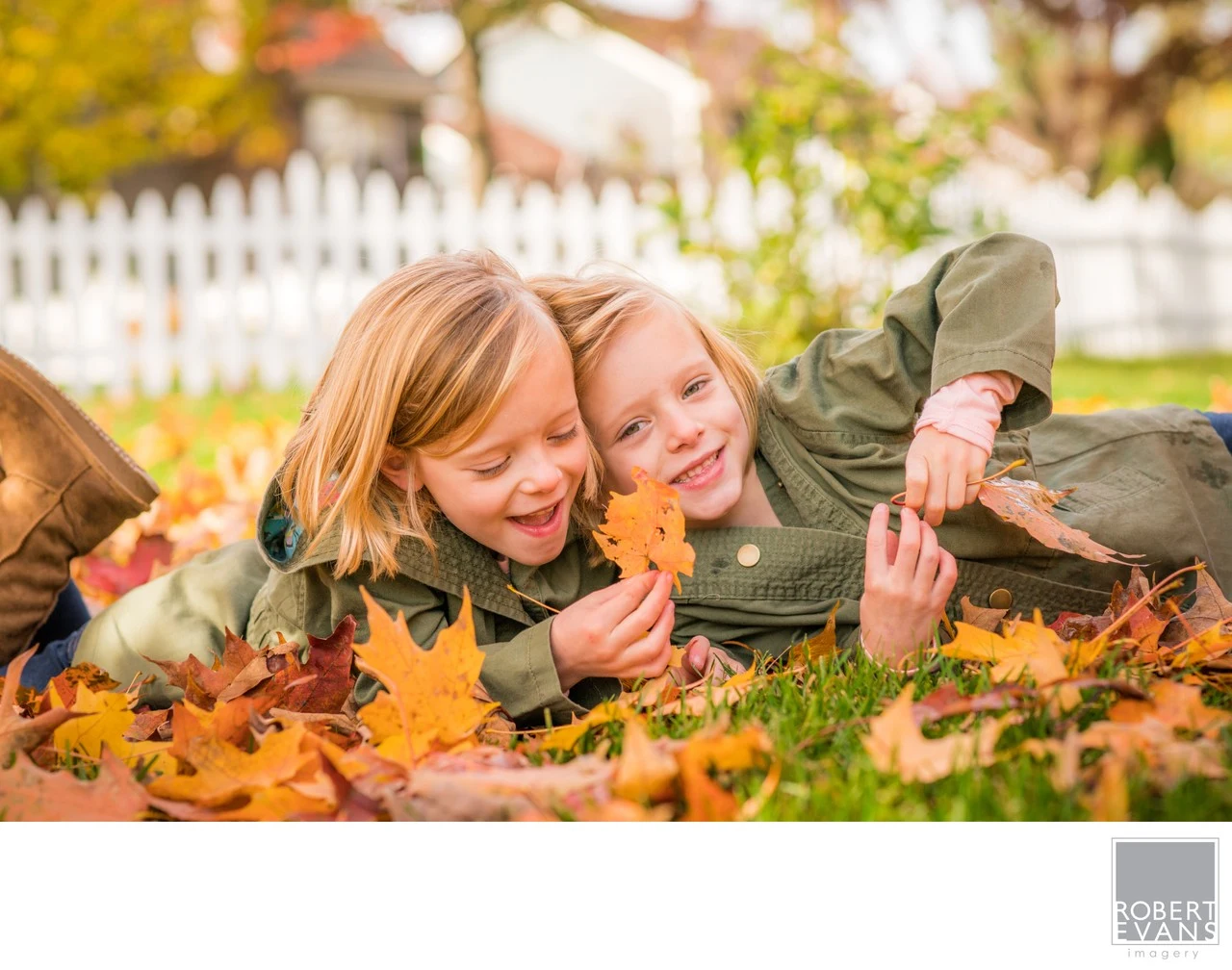 Two children lie together in fallen leaves, laughing during a playful outdoor portrait.