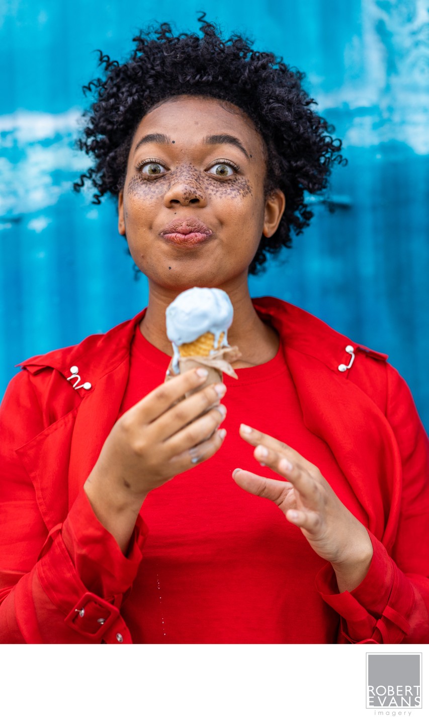 A woman in a bright red top holds an ice cream cone against a blue background.