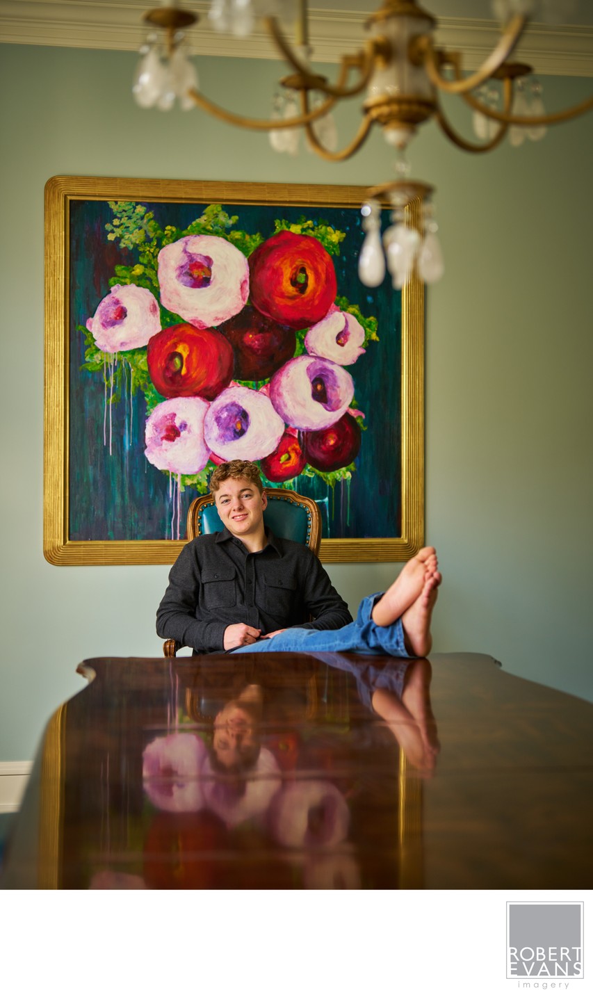A young woman rests at a table beside a reflection of floral artwork.