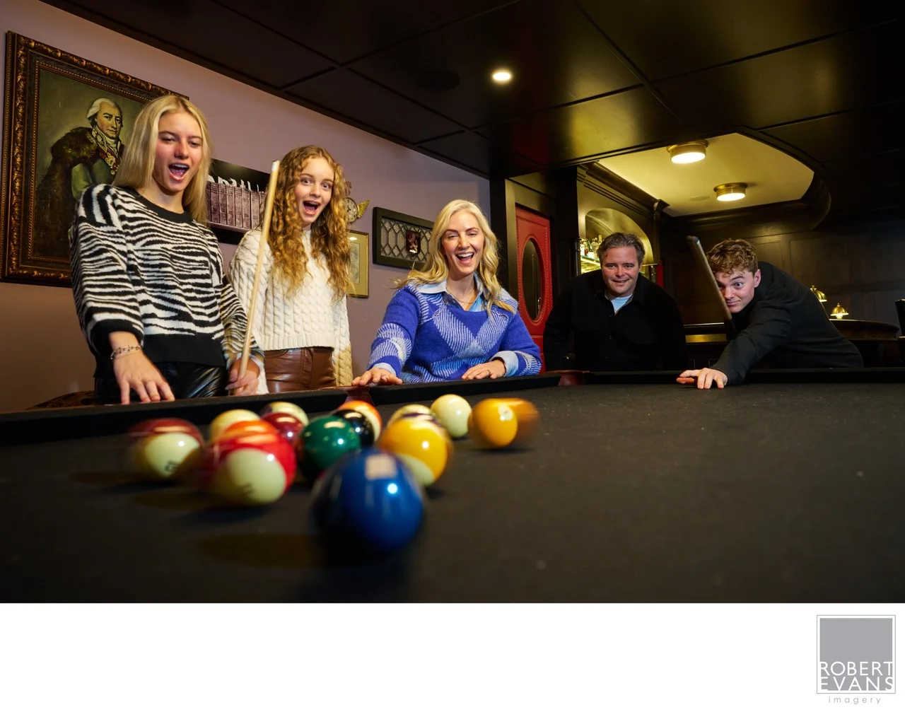 A family gathers around a pool table at home.