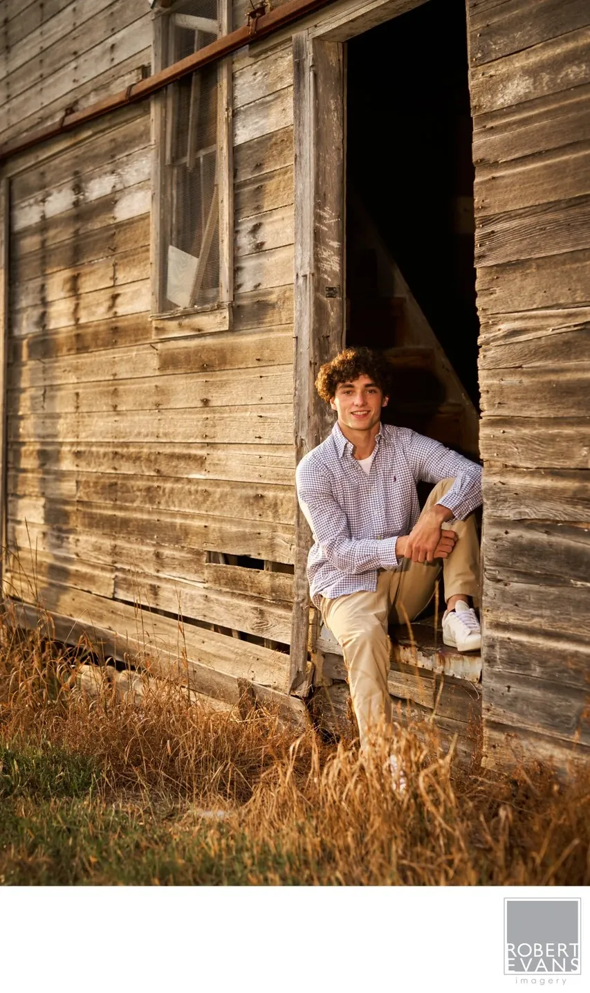 A young man sits in a rustic barn doorway.