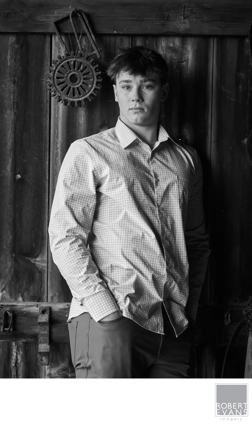 A young man in a button-down shirt poses beside a weathered wall in black and white.