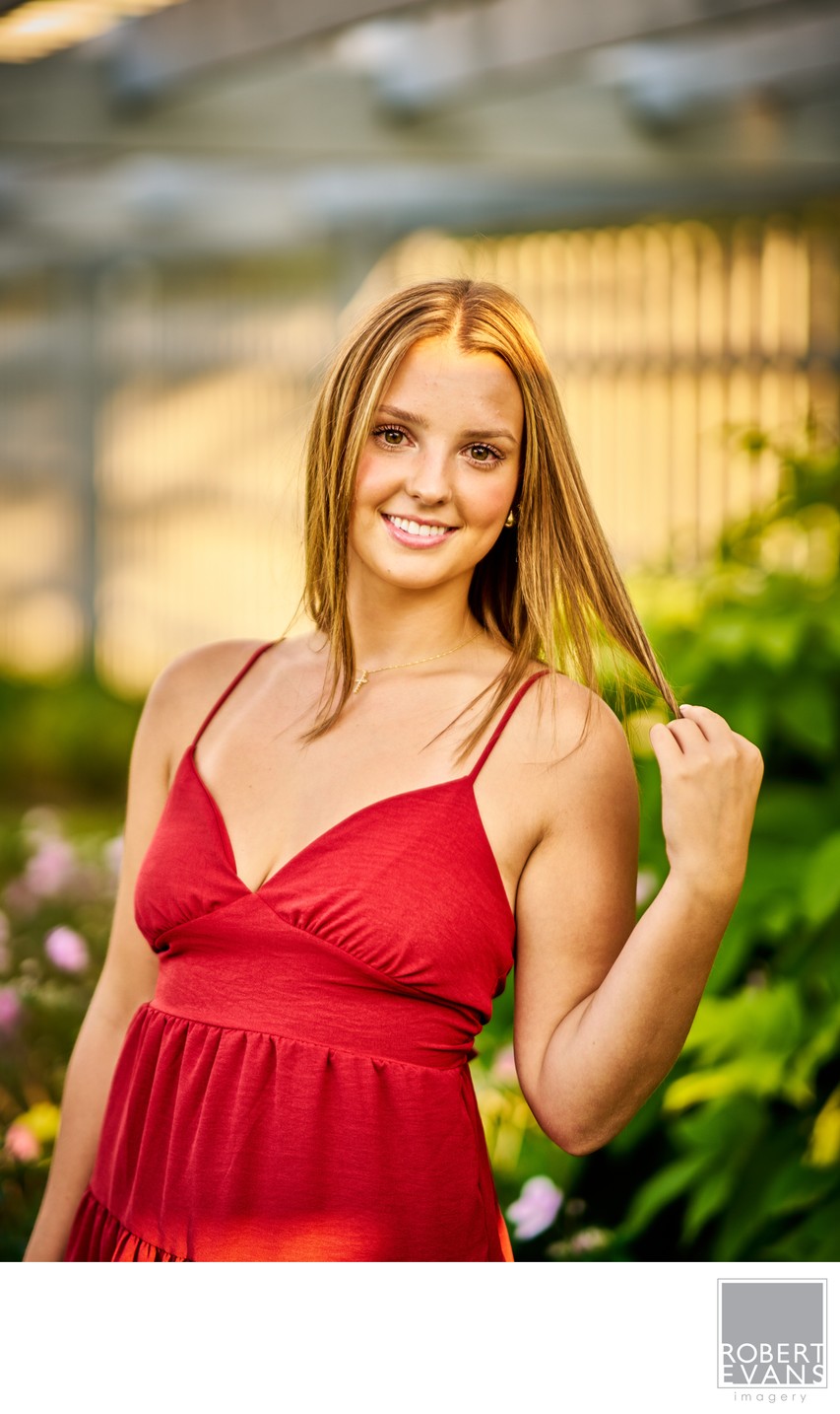 A smiling young woman wears a red dress in an outdoor portrait.