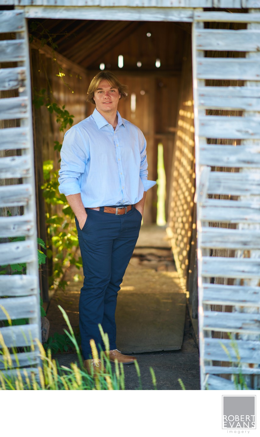 A young man in a blue shirt stands at a rustic doorway beneath string lights.