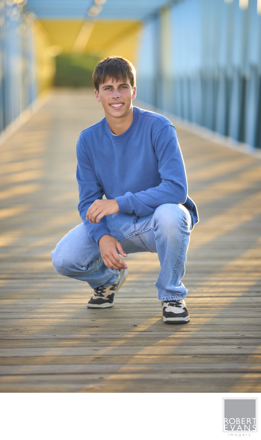 A young man in a blue sweater crouches on a steel bridge.