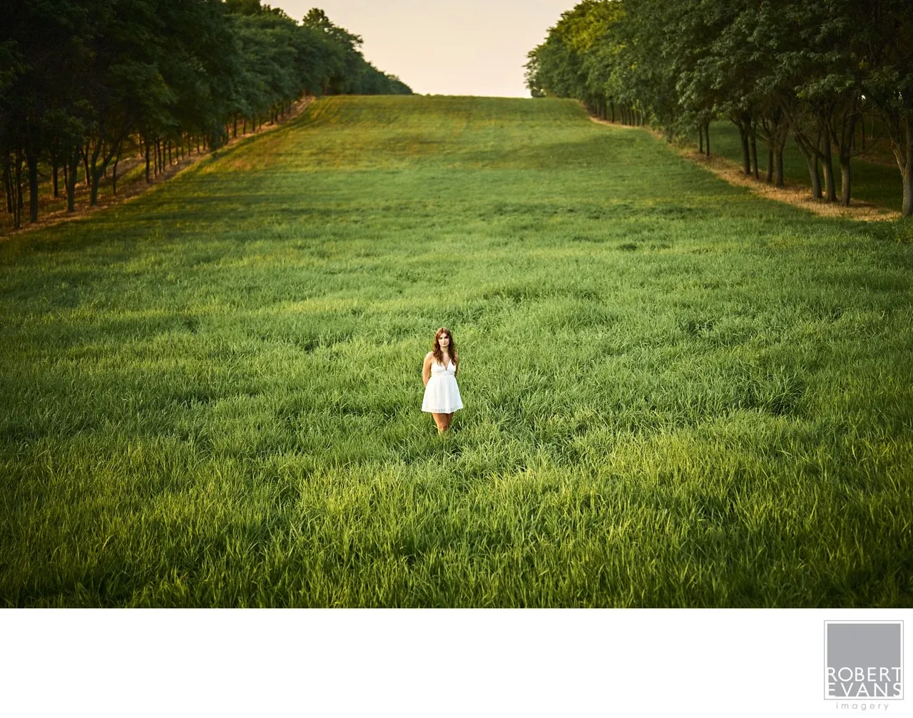 A young woman in a white dress stands in a green field.