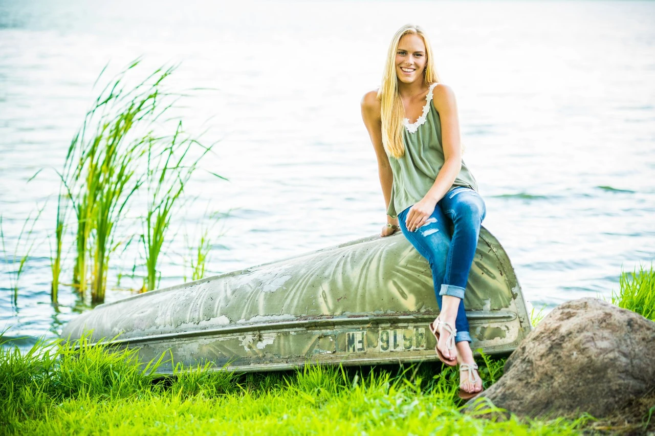 A young woman in a green top and jeans sits in a canoe on a lake.