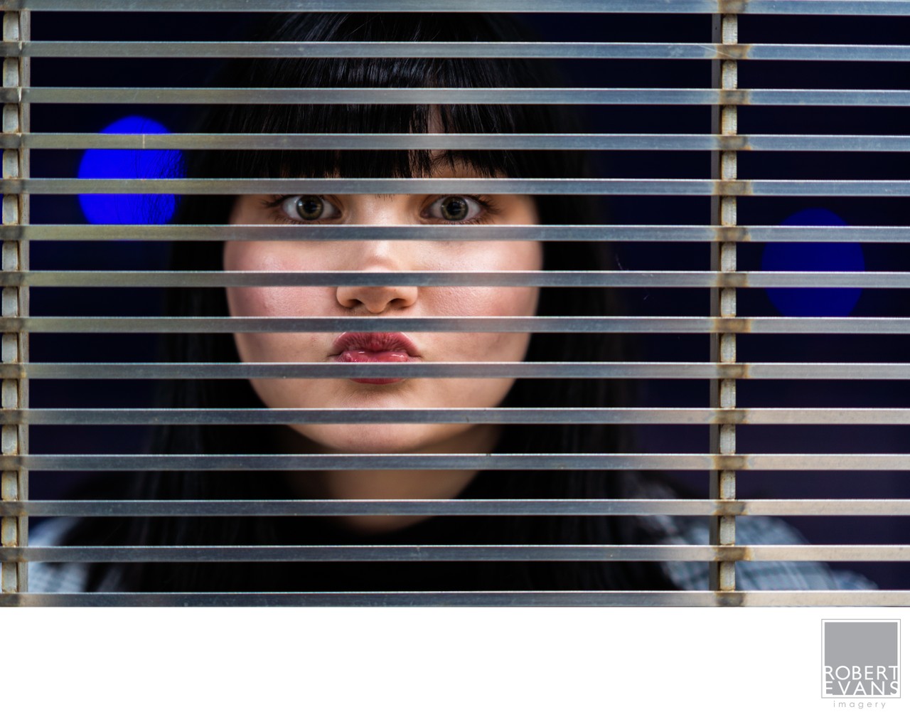 A young woman's eyes appear between horizontal window blinds.