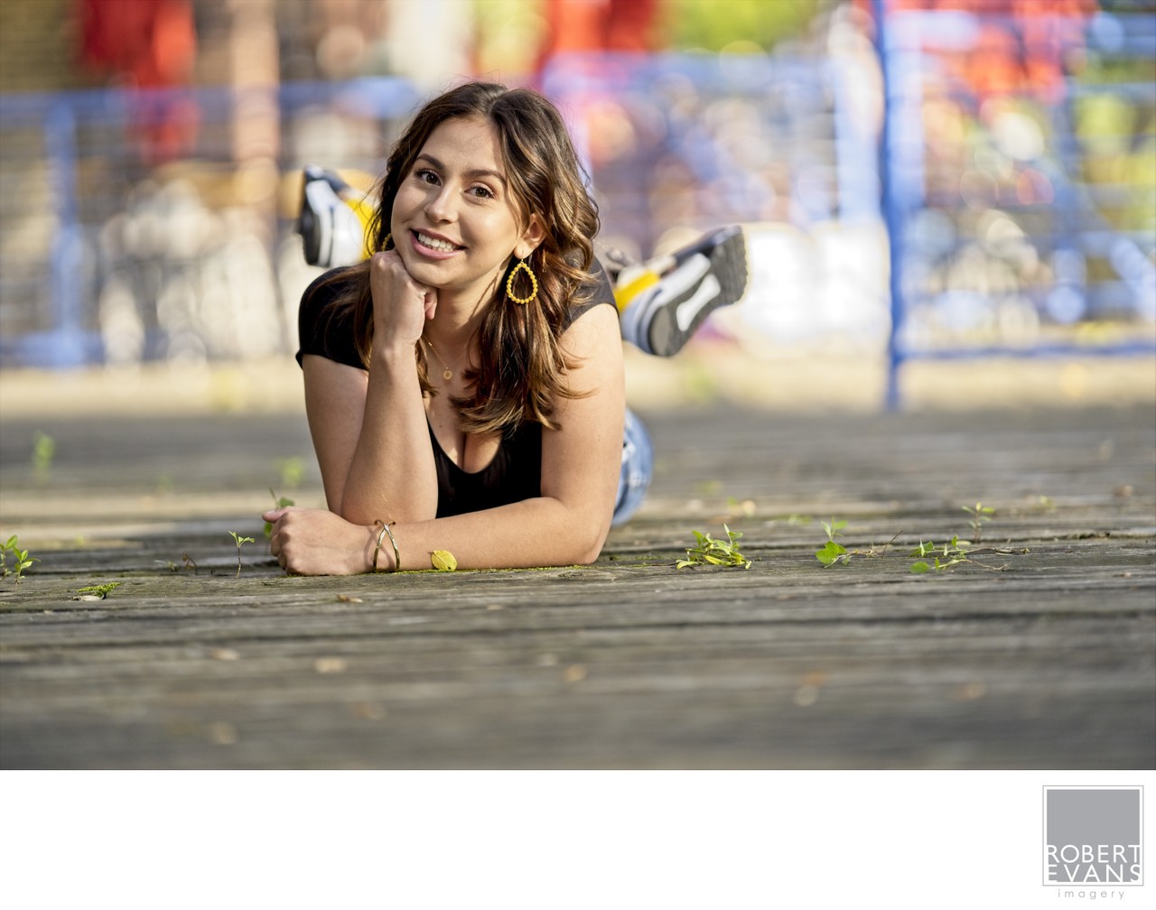 A young woman lies on a wooden walkway with colorful graffiti behind her.