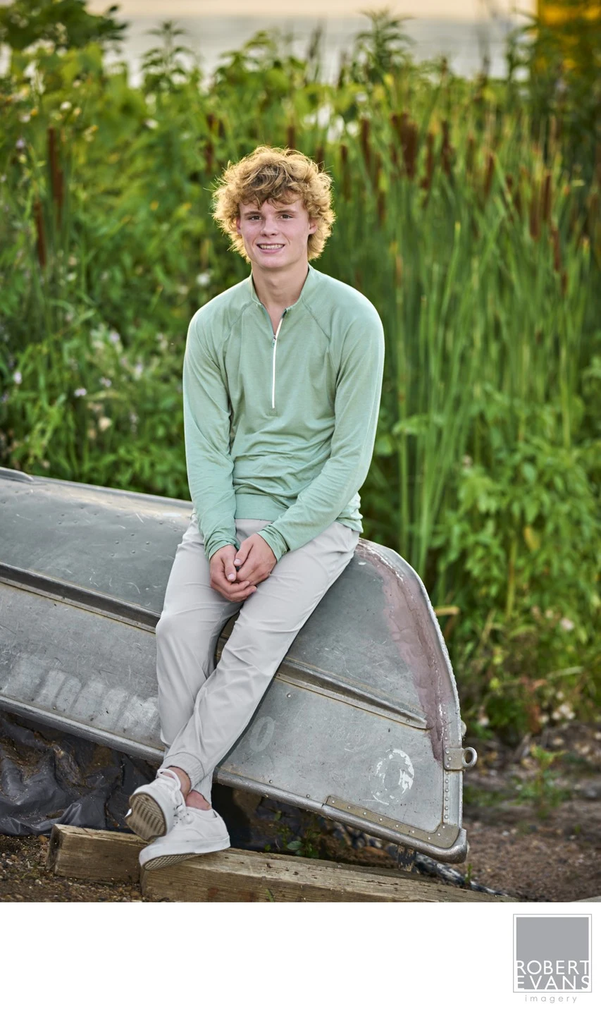 A young man in a green shirt sits in a canoe surrounded by reeds.