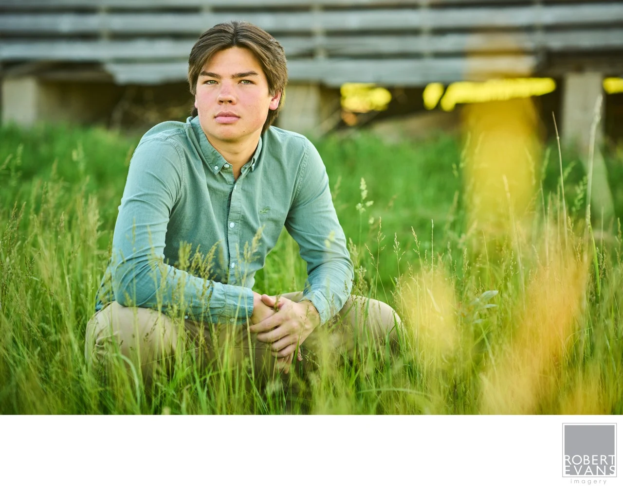 A young man in a green shirt sits in the grass.