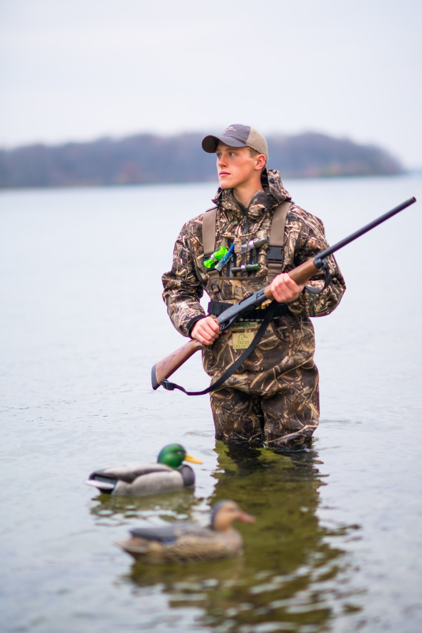 A young man wearing camouflage stands in water among duck decoys.