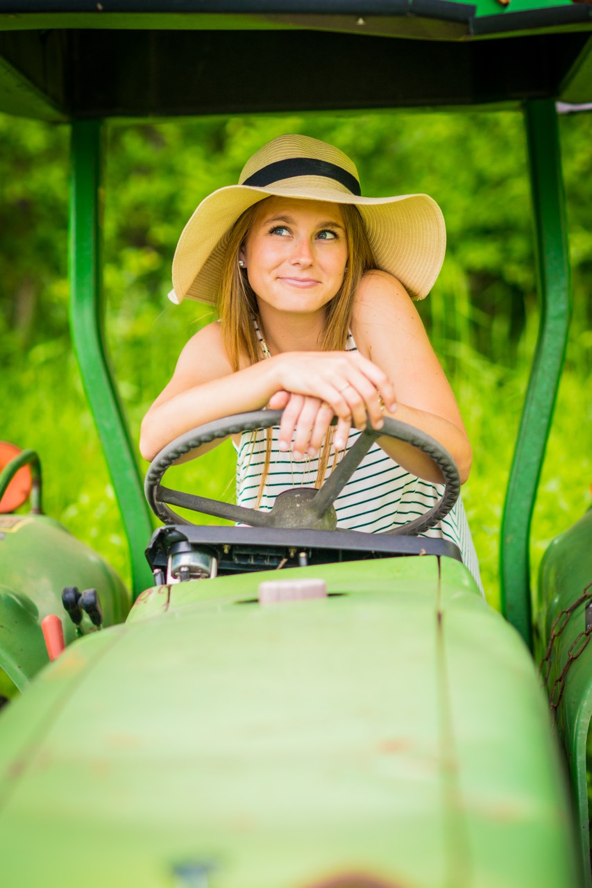 A young woman in a hat sits on a green tractor.