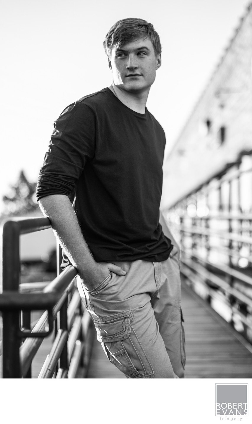 A young man in a black sweater leans at a bridge railing in black and white.