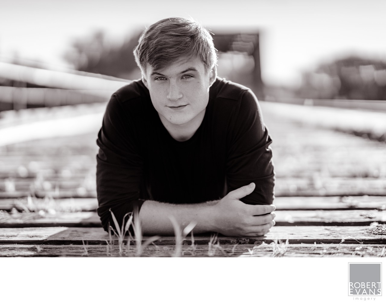 A young man rests on a wooden walkway in a black-and-white portrait.