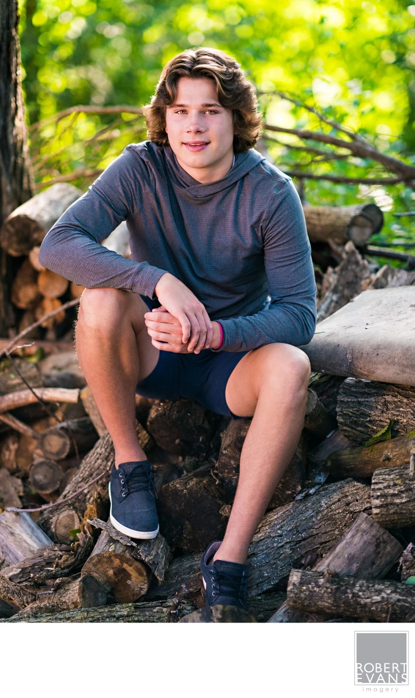 A young man in a gray shirt sits among exposed roots and rocks.