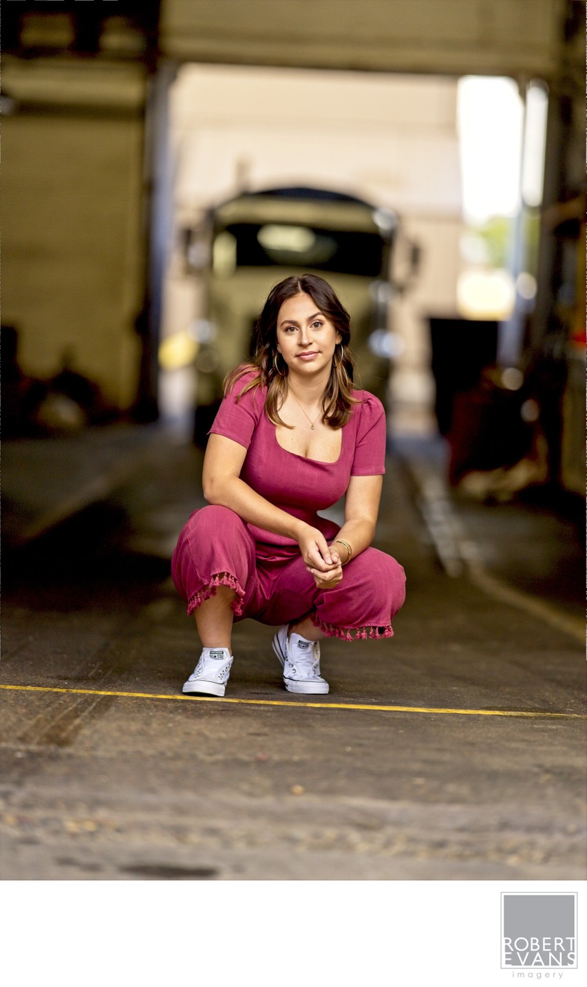 A young woman in a pink dress crouches in a shadowed urban passage.