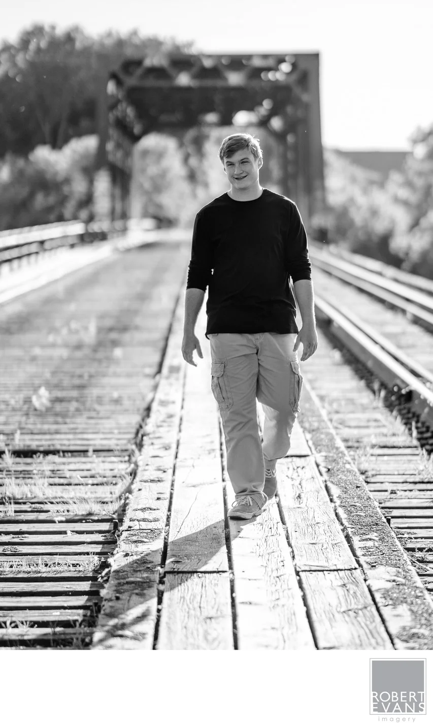 A young man walks along a wooden bridge in black and white.