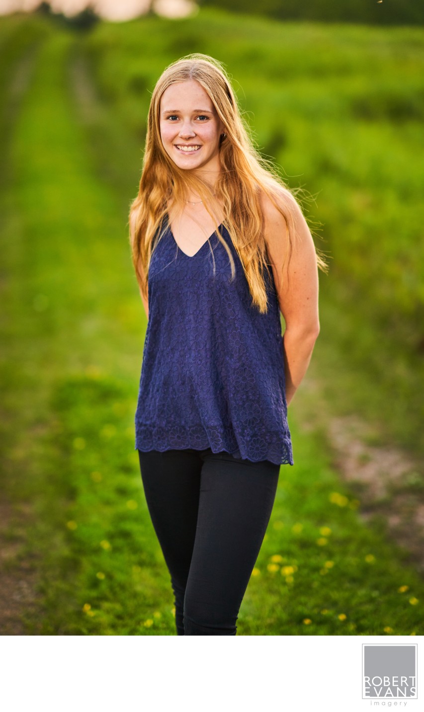 A smiling young woman in a blue top stands in a green meadow.