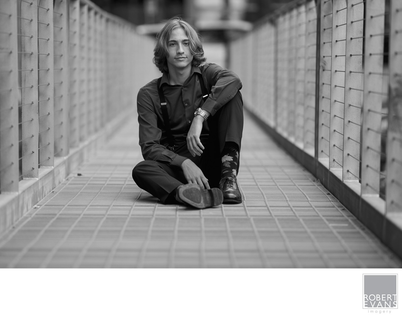 A young man sits cross-legged on a metal walkway in black and white.
