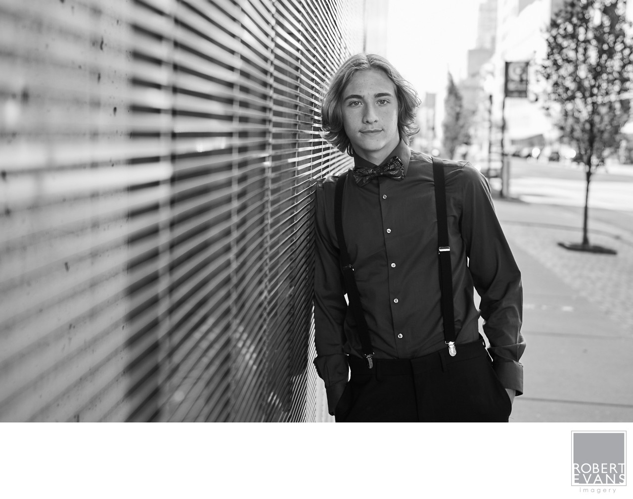 A young man in a dark shirt stands beside a textured city wall in black and white.
