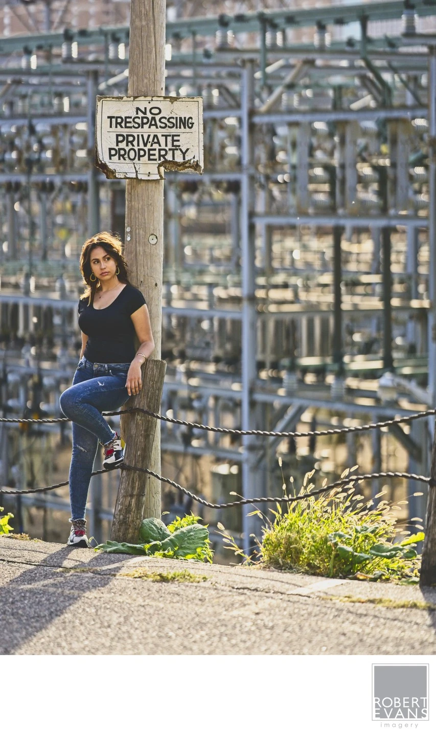 A young woman in a dark top and jeans stands beside an ornate iron gate.