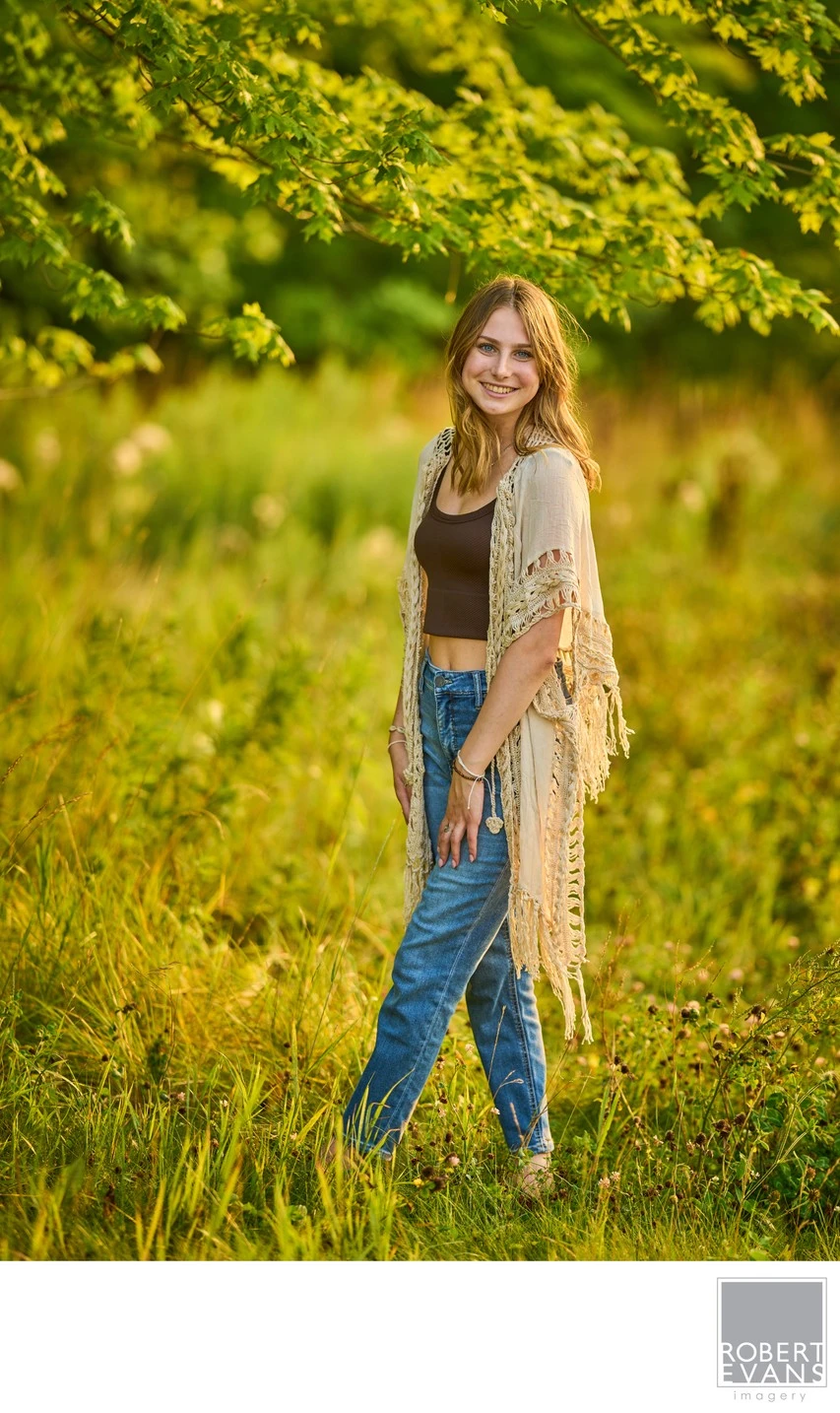 A young woman wearing jeans and a light shawl stands among meadow grasses.