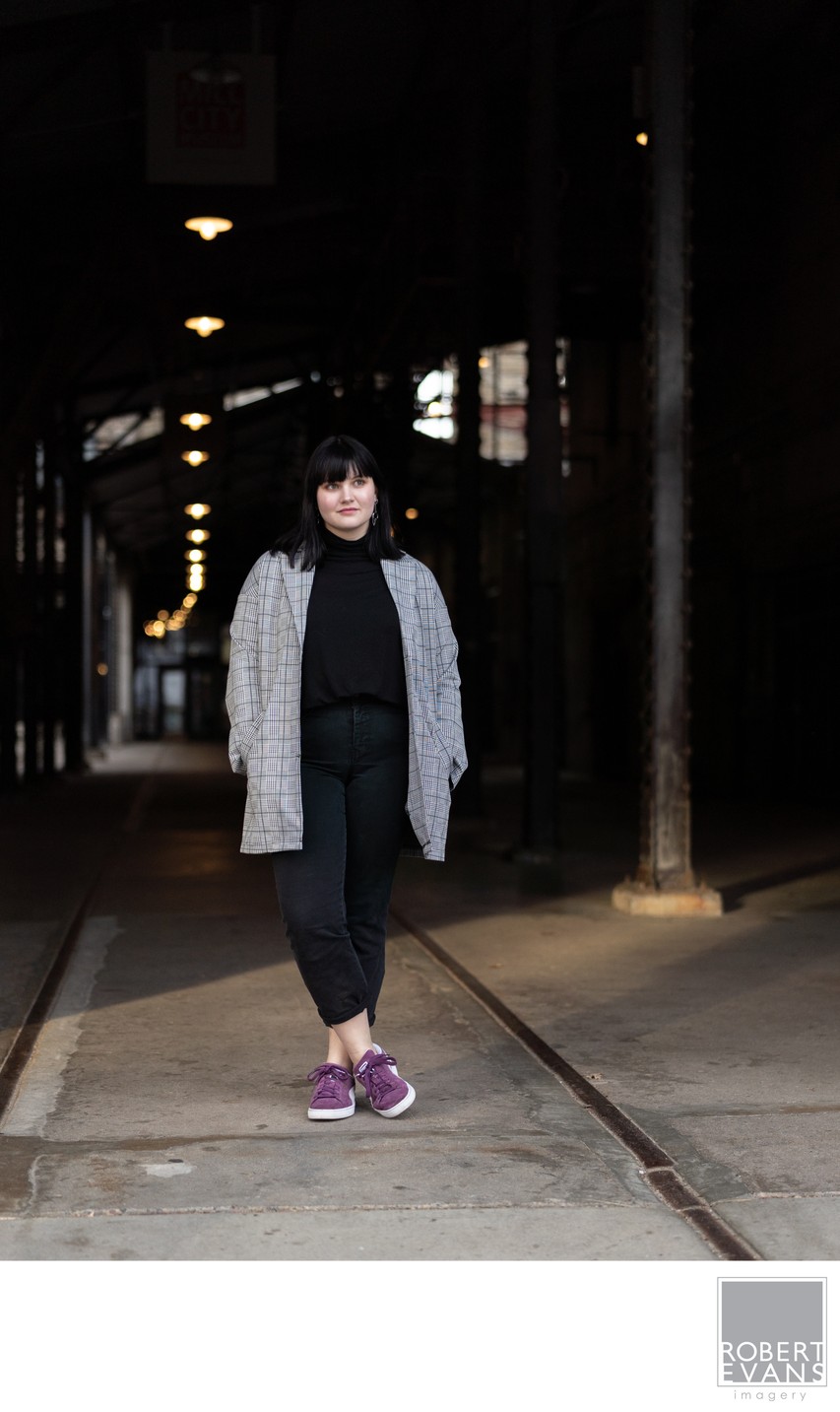 A young woman in a gray coat walks through a dark urban passage.