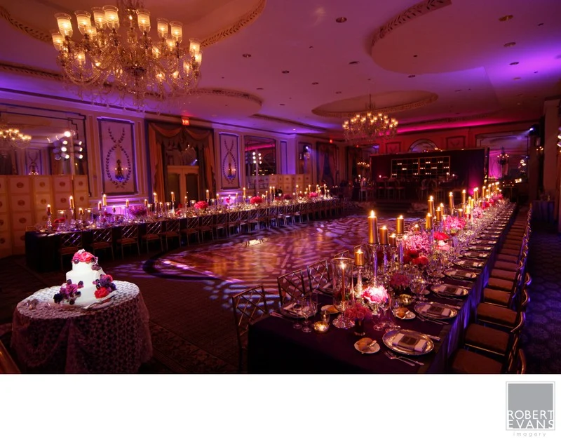 A reception room with long tables, candles and purple lighting.