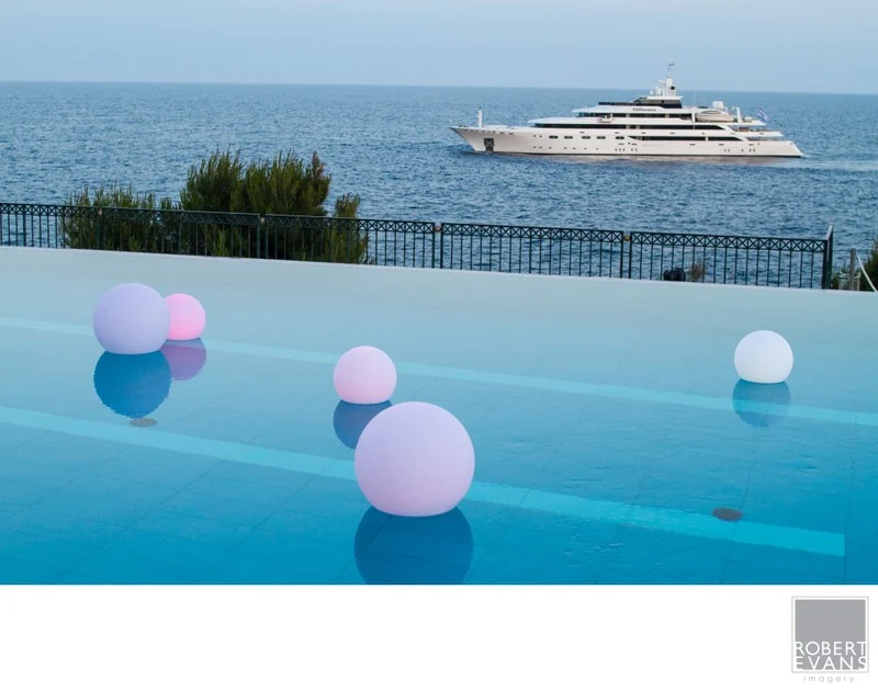 A swimming pool decorated with glowing spheres overlooking the sea and a boat.