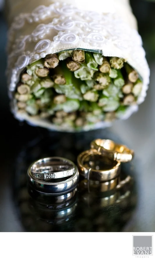 Wedding rings beside the ribbon-wrapped stems of a bridal bouquet.