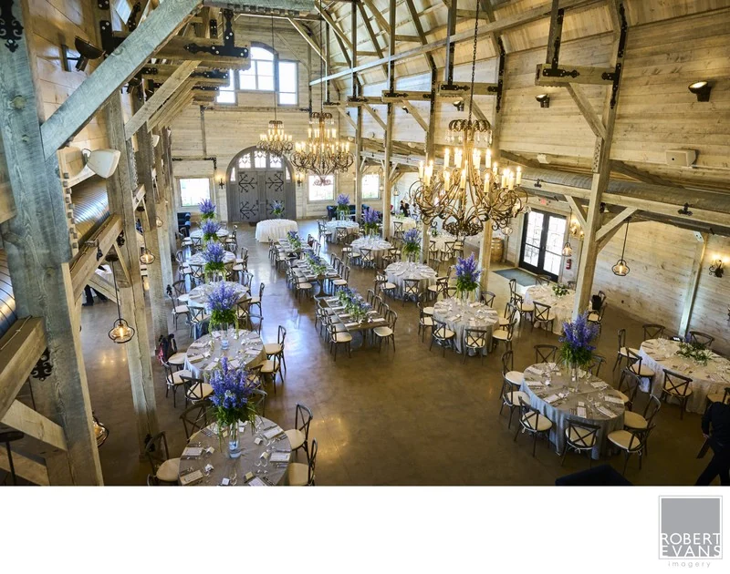 An elevated view of reception tables and floral arrangements beneath exposed timber beams.