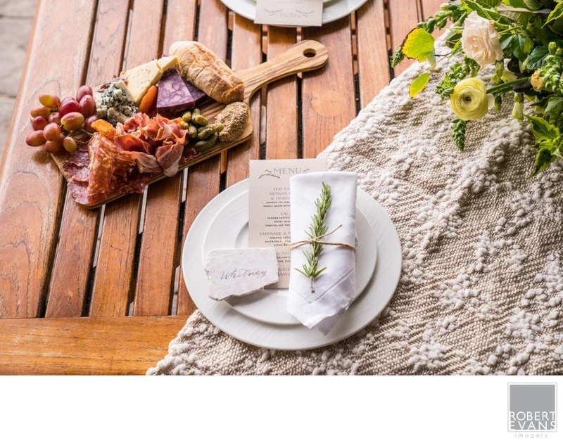 A white place setting with a green sprig beside a grazing board and soft table runner.