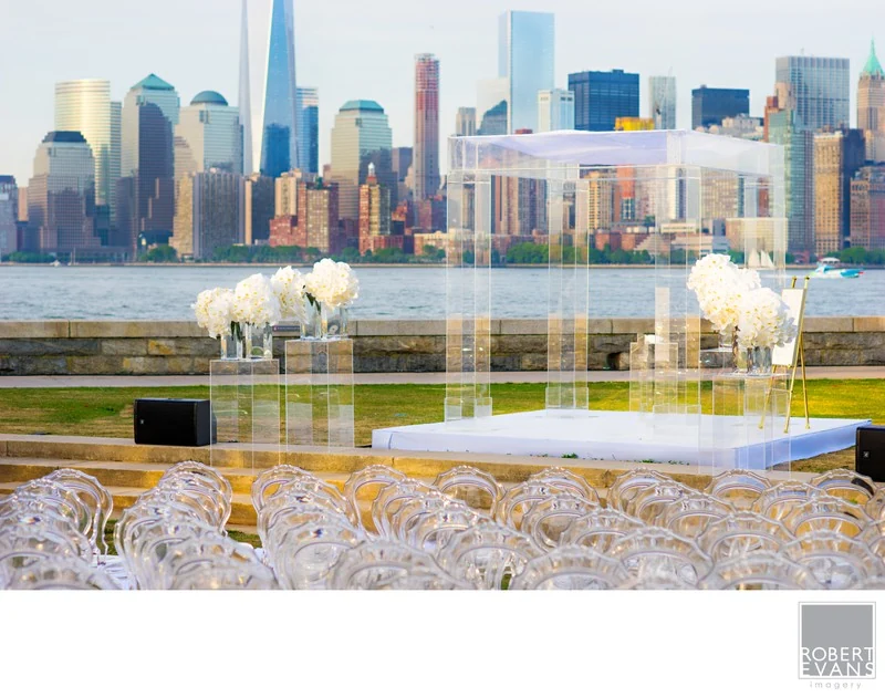 A wedding reception table set with glassware and white flowers beside windows overlooking a city skyline.
