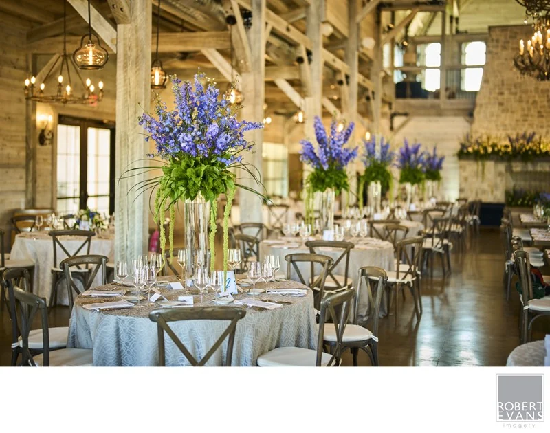 Blue floral centerpieces and candles on reception tables in a rustic timber room.