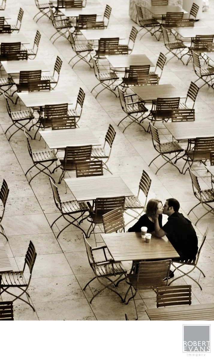 A couple kissing at one table among rows of empty café tables.