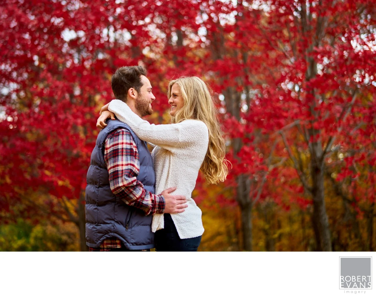 A couple embracing beneath brilliant red autumn leaves.
