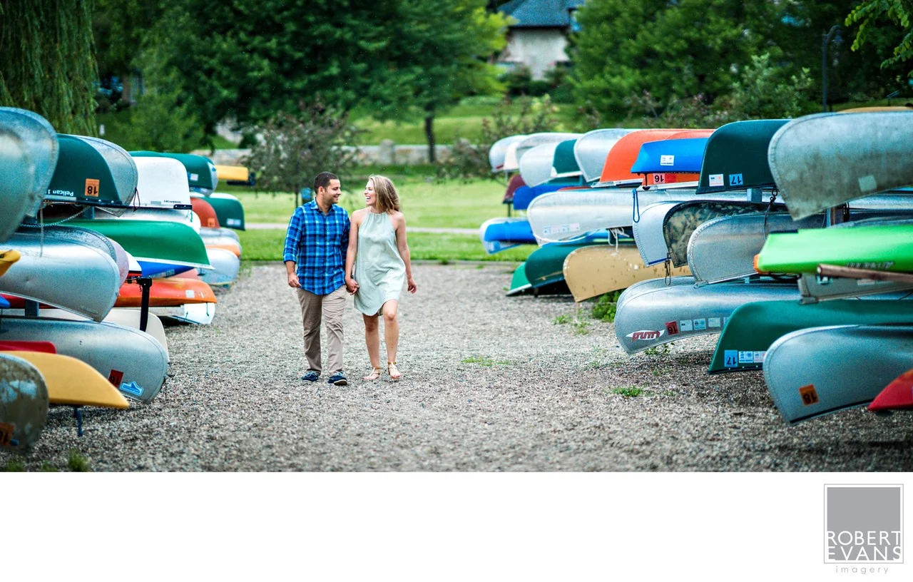 A couple walking hand in hand between colorful racks of canoes.