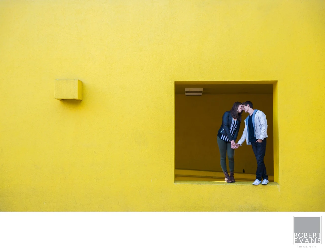 A couple standing together in a recessed doorway in a vivid yellow wall.