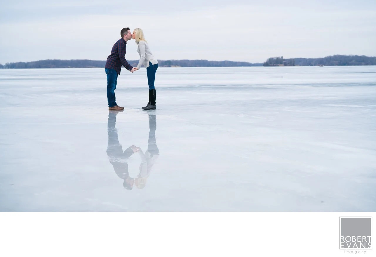 A couple facing each other on a frozen lake, their reflections visible beneath them.